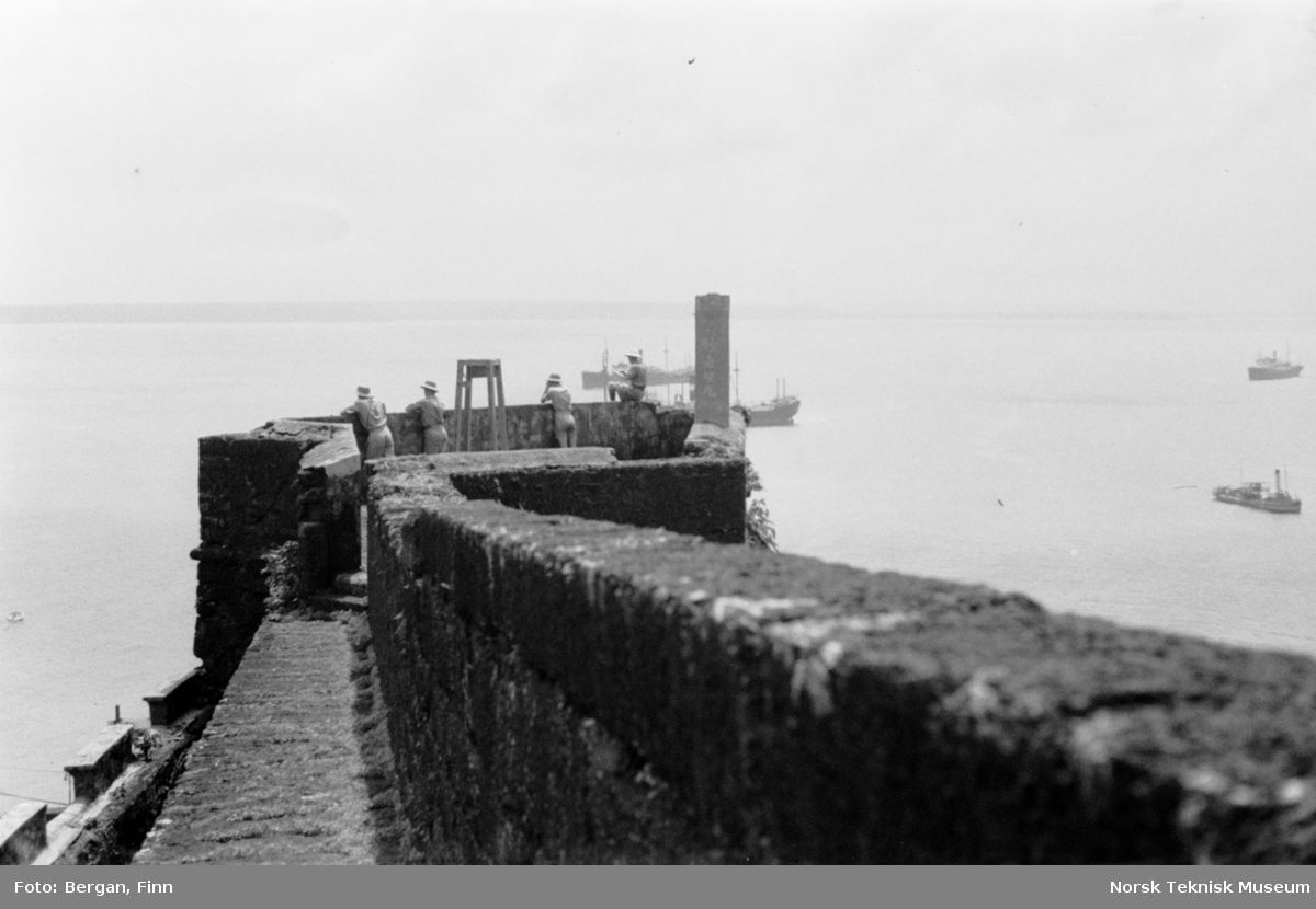 Festningsmur ut mot sjøen, fire personer på muren