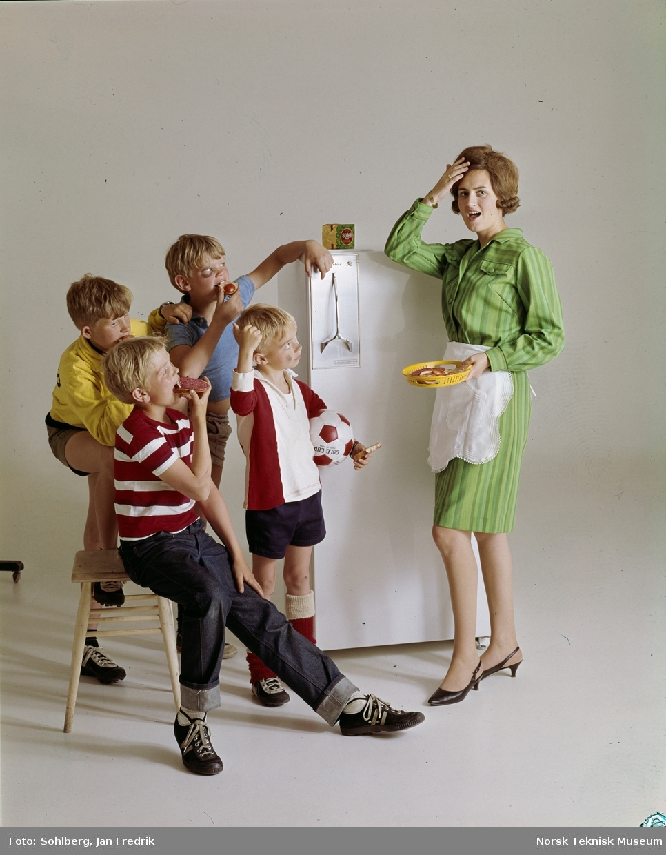 Et humoristisk reklamefoto; en kvinne / mor / husmor står ved kjøleskapet med hånden for pannen og et lett fortvilet uttrykk. Rundt henne er fire sultne gutter, med fotballutsstyr og noen blåmerker. De spiser.