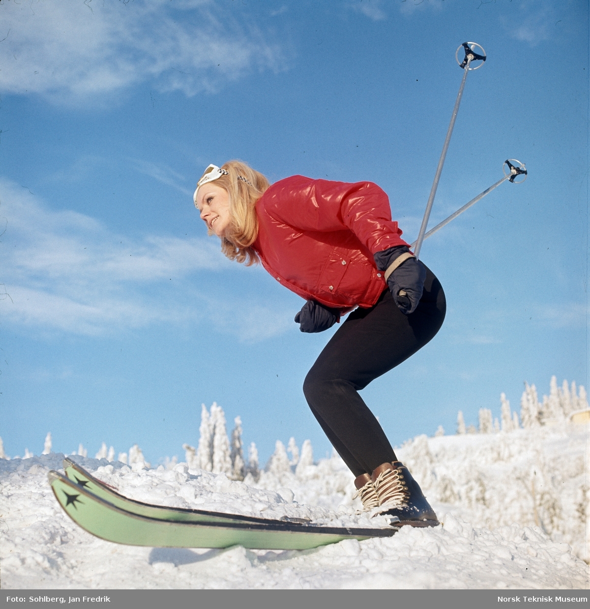 Skimote. En kvinnelig modell på ski. Hun har rød jakke og slalombriller.