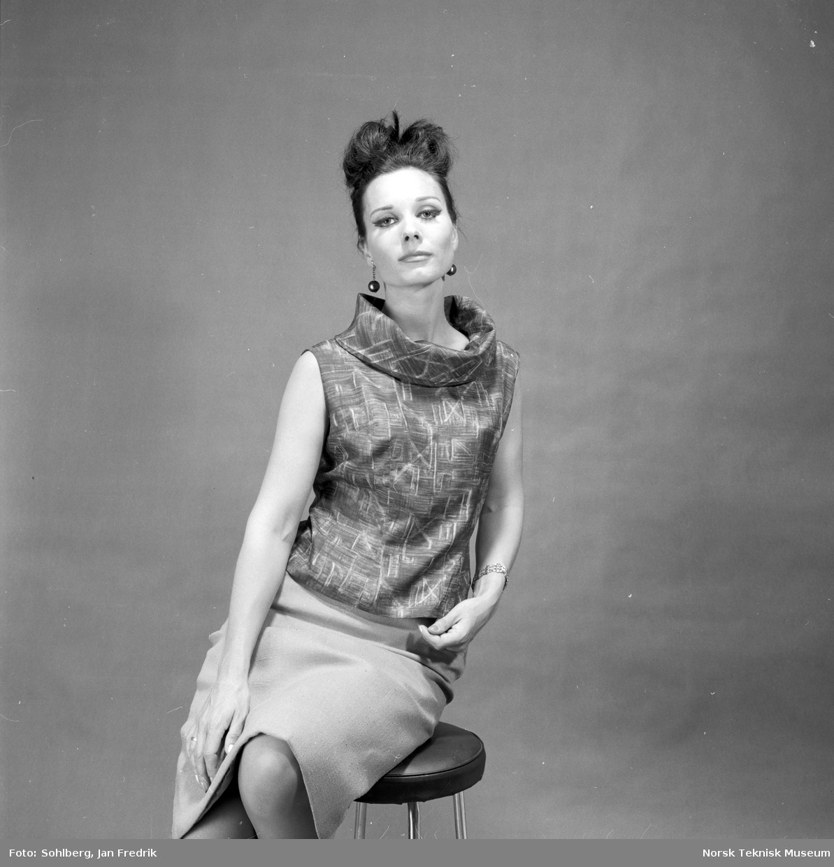Kvinnelig modell i kortermet topp og skjørt.  Fra artikkel i Norsk Dameblad. nr. 35, 1963, v/ Kirsten L . kalt "Ute inne borte".