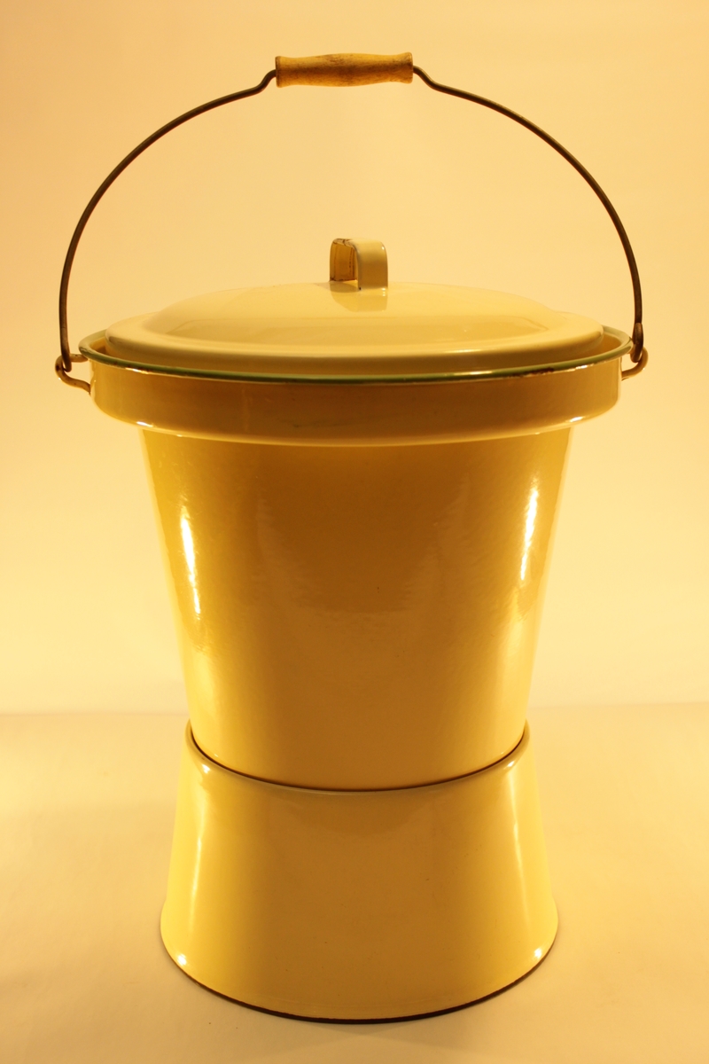Emaljerad plåtpotta gul med gröna kanter. Pottan är i form av en hink med lock. Innanför locket ett sittring av trä. Hinken har även ett handtag med handgrepp i trä