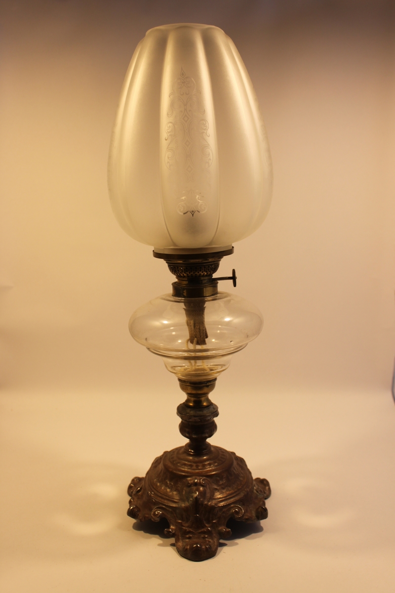 Fotogenlampa på mässingsfot i nyrokokostil. Kupan med sk tulpanform i frostat glas med snirklig dekor.