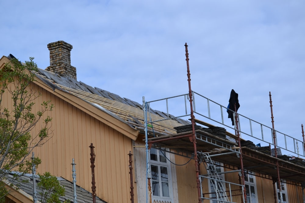 Leirfjord, Nedre-Leland. Entreprenørfirmaet, Einmo, legger om taket på Bergh-brygga (museet). Stillas på sjøsiden. Taksteinen er tatt ned, ny papp lagt på og det er lagt på lekter. Her skal skifersteinen festes.
