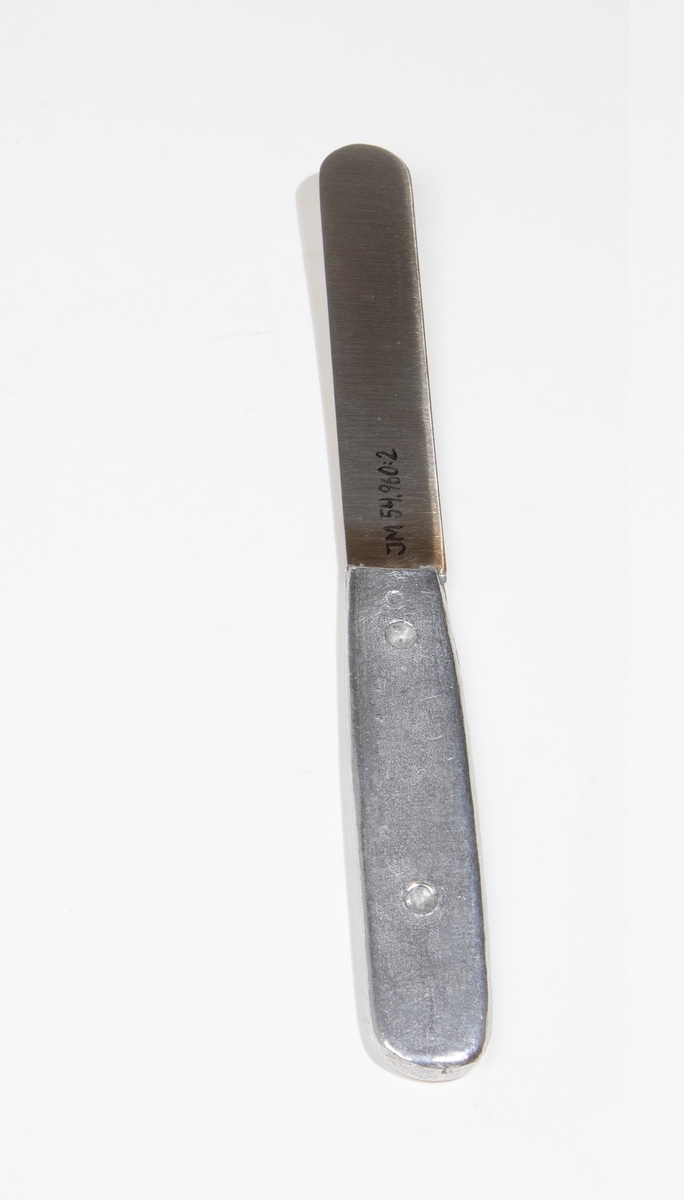 Kniv av lättmetall. Hör ihop med sked (JM 54960:1), gaffel (JM 54960:3) och förpackning (JM 54960:4). Stämplad: "ROSTFRITT STÅL BAS".