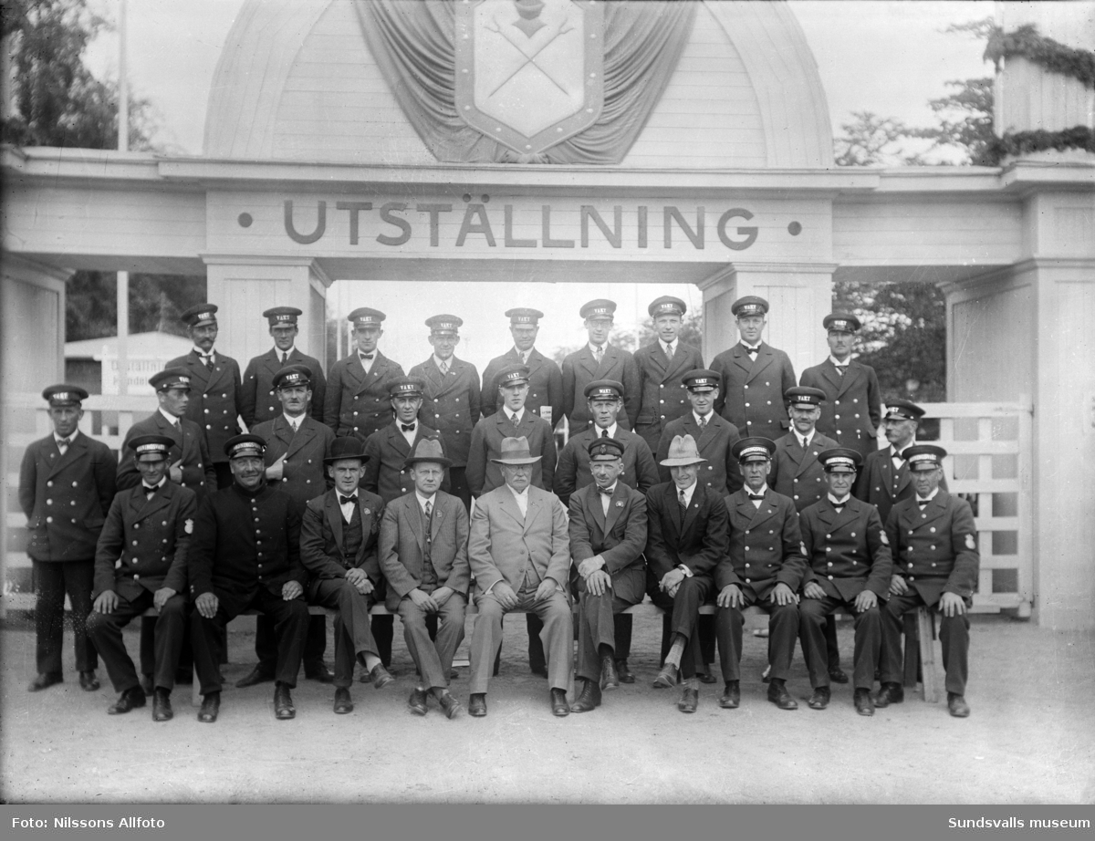 Grupporträtt vid entrén till Sundsvallsutställningen 1928. Vaktpersonal och styrelse.