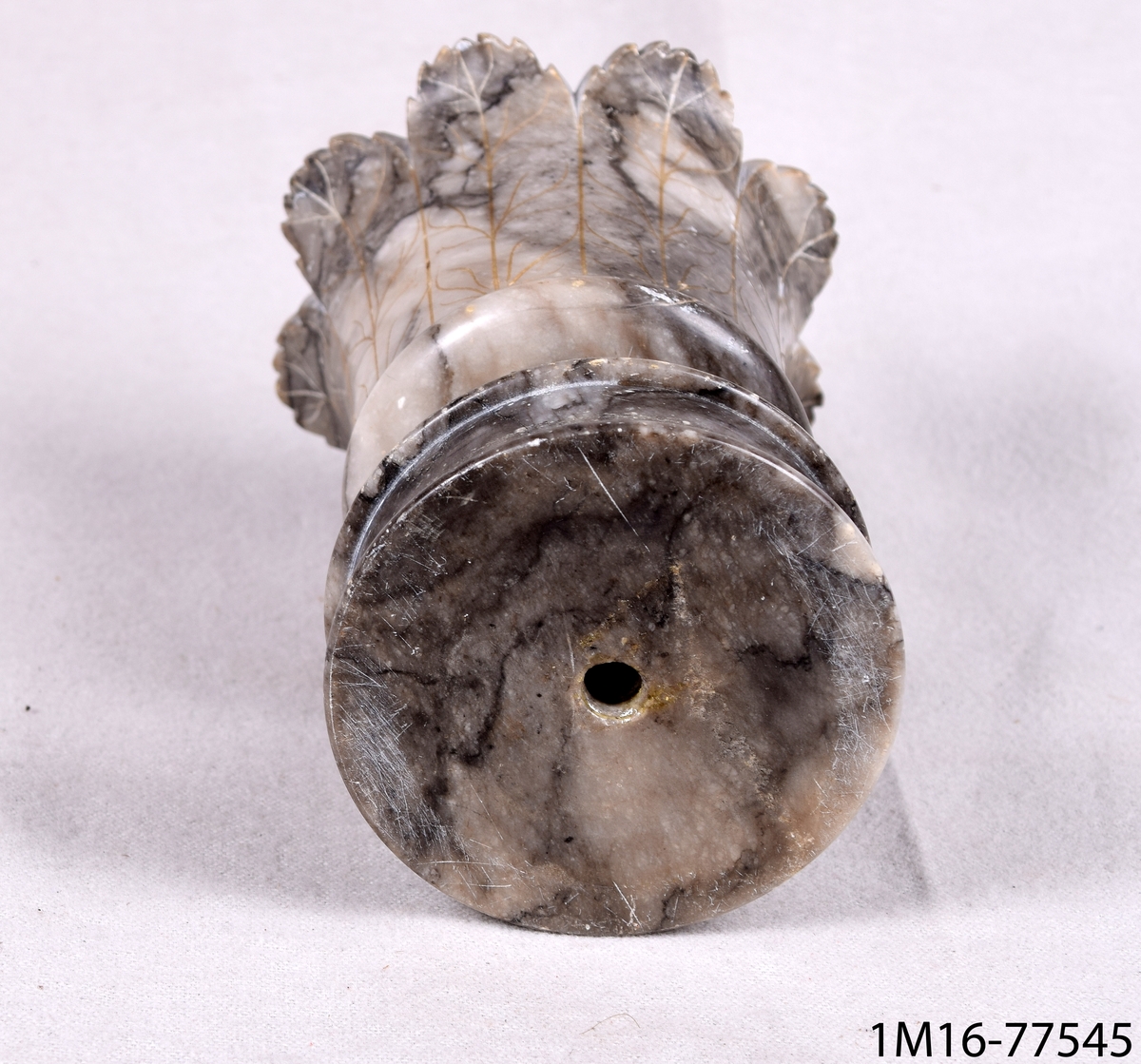 Cigarrställ av gråflammig marmor. Stället har en rund fot och i övre kant, vid mynningen, flikig blombladsliknande dekor.