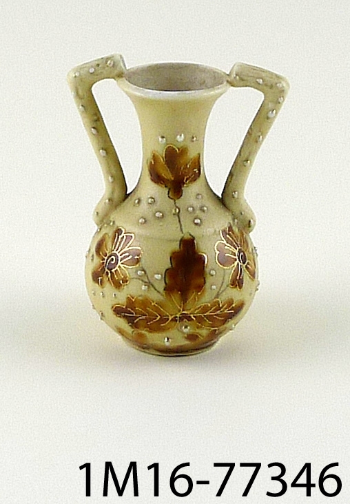 Rund vas av porslin, grågul botten, blommor i brunt, detaljer i guld, vasen har två öron.