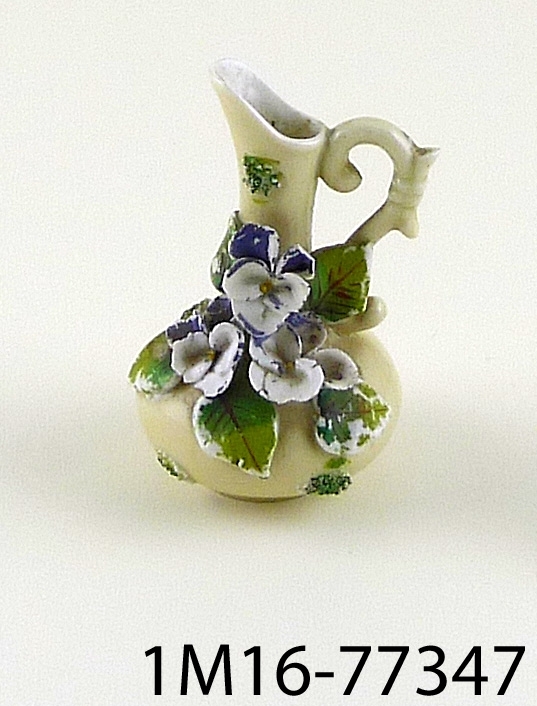 Rund vas av porslin, vid nedtill, långsmal hals, ett öra, modellerade blommor  (violer eller penséer) på sidan. Handmålad dekor på detaljer.