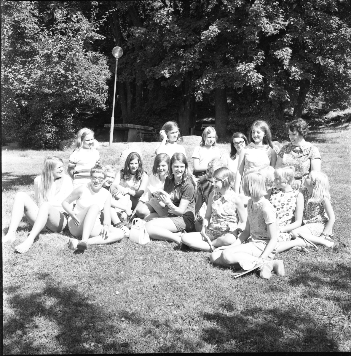Sommarklädda flickor sitter på gräsmattan i Grännaskolans trädgård.