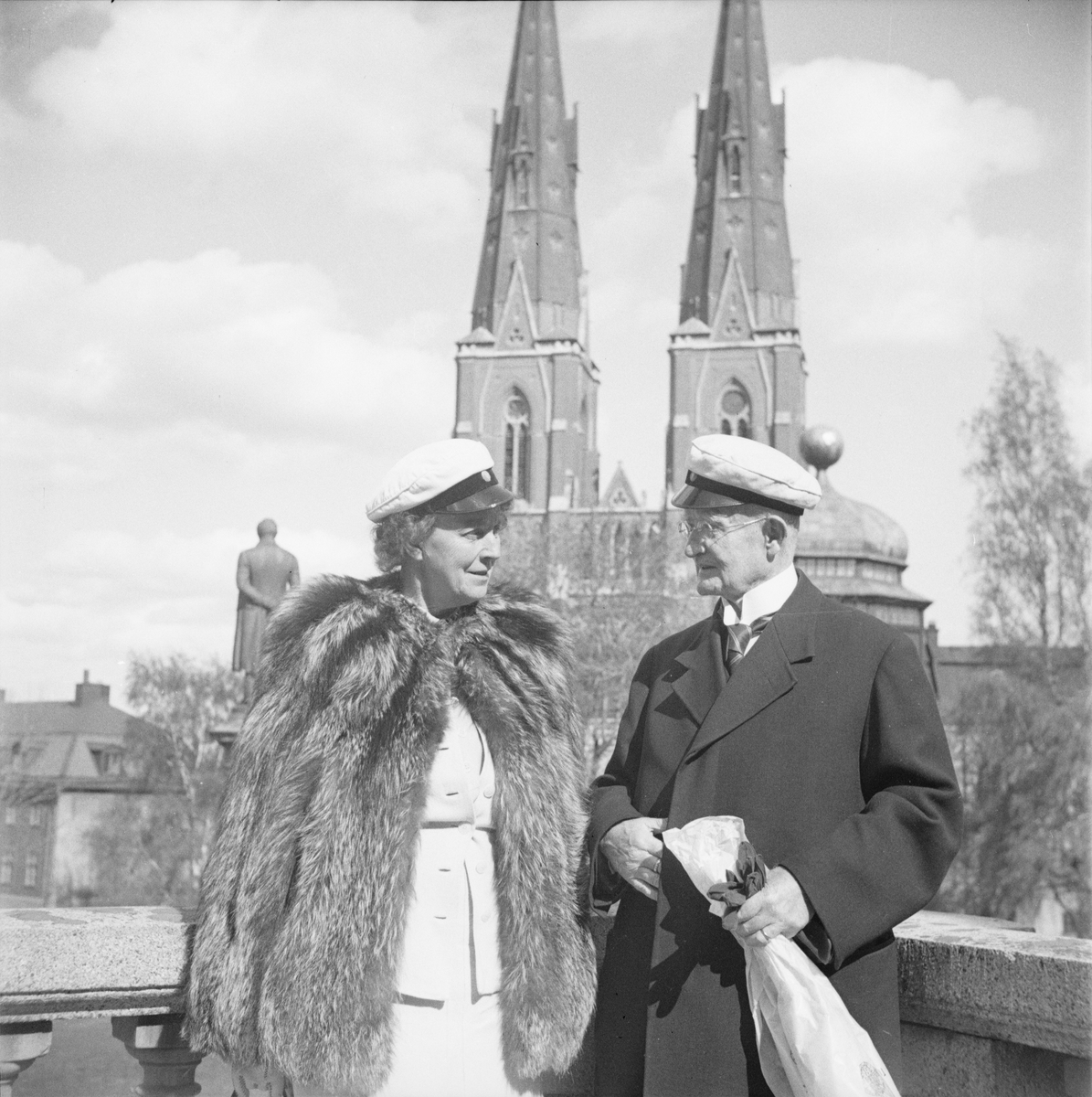 En man och en kvinna med studentmössa, i bakgrunden Uppsala domkyrka, Östgöta nations minneslandskap, Uppsala 1949