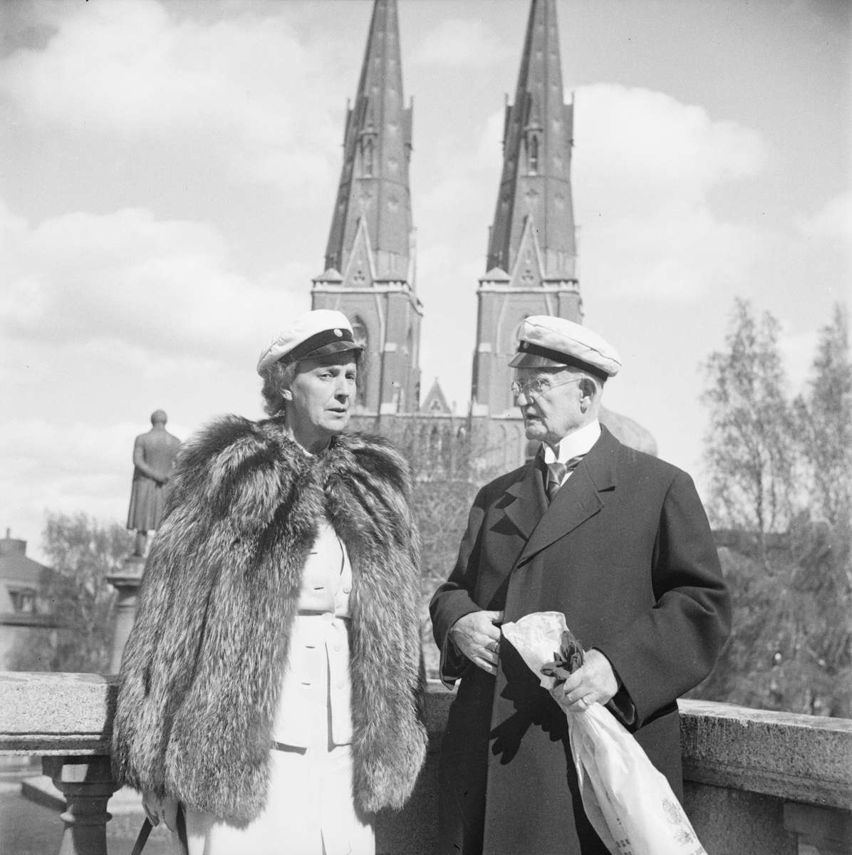 En man och en kvinna med studentmössa, i bakgrunden Uppsala domkyrka, Östgöta nations minneslandskap, Uppsala 1949