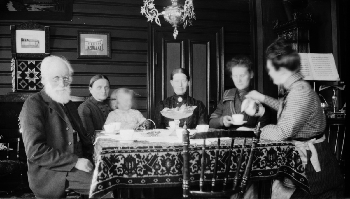 Fem voksne og ett barn rundt kaffebordet, antakelig på Linjordet i Østre Gausdal
