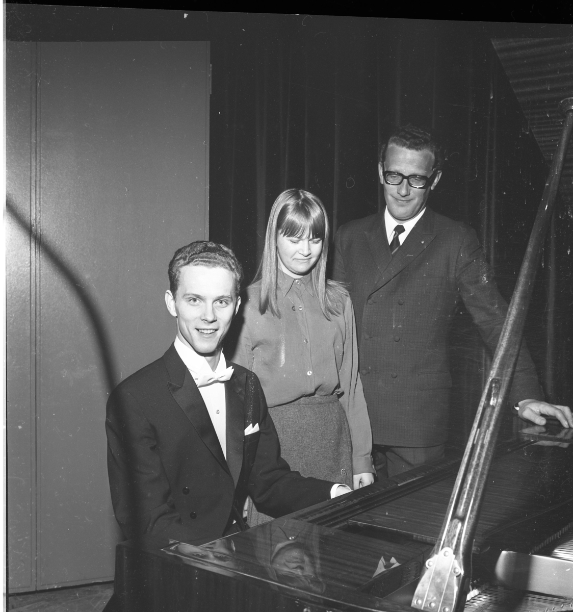 Pianisten Lars Roos i frack sitter vid en flygel, ler mot fotografen. Intill står Katarina Ivarsson och Sten Sarborn.