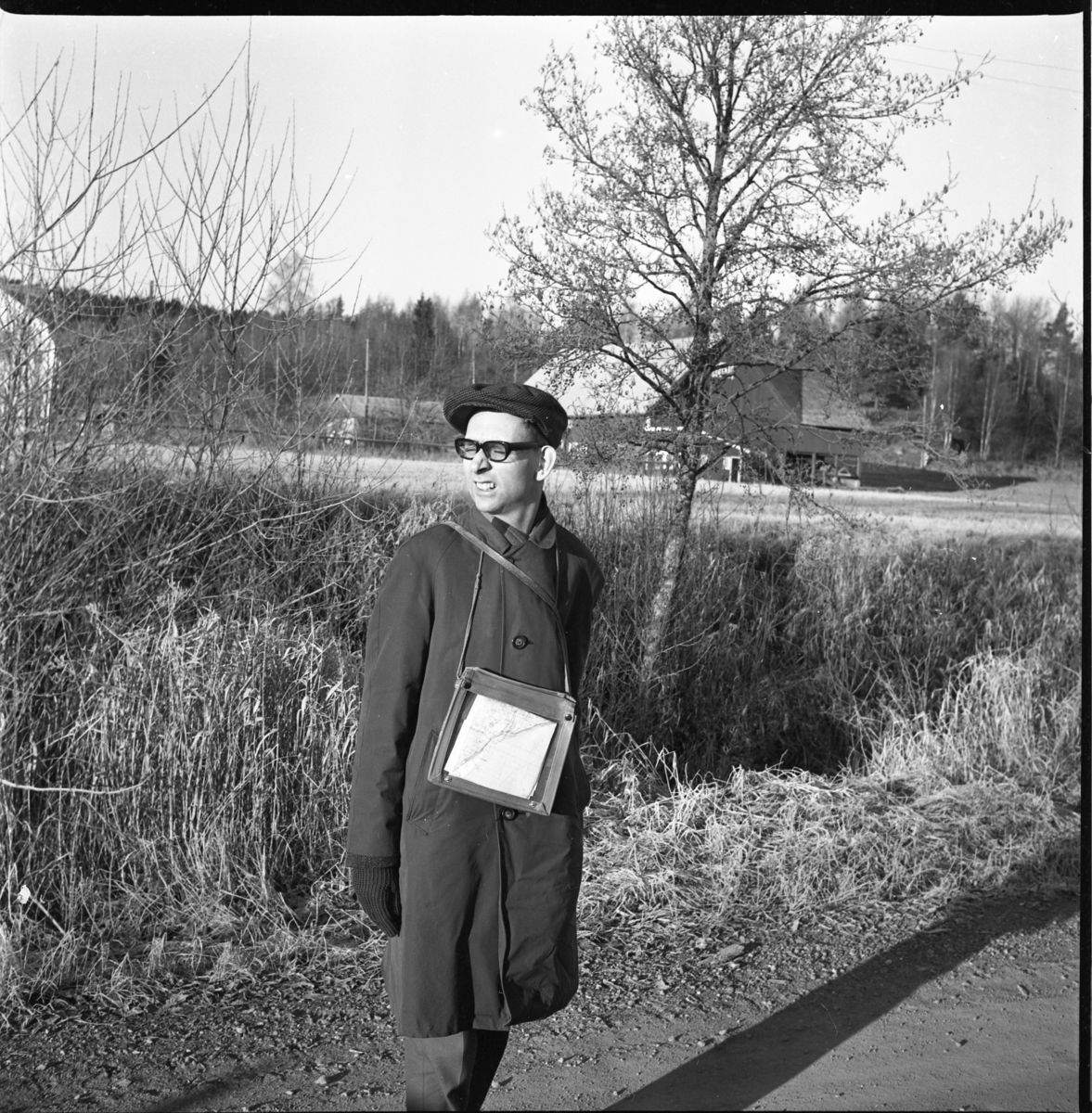 Långvandraren Olof Tynell från Stockholm står på en grusväg. Han har keps och rock. Runt halsen hänger ett kartfodral med karta i. Han kisar då han har solen i ögonen.