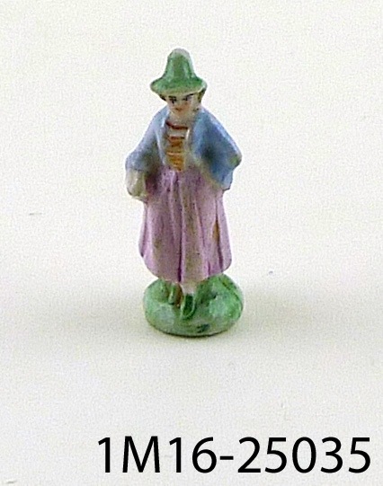 Figurin föreställande kvinna i grön hatt och skor, gult och rött livstycke och rosa kjol samt blå sjal.