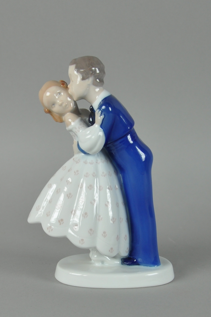 Skulptur av glassert keramikk, med fargedekor. Skulpturen forestiller gutt som kysser jente på kinnet. Skulpturen står på en oval sokkel.