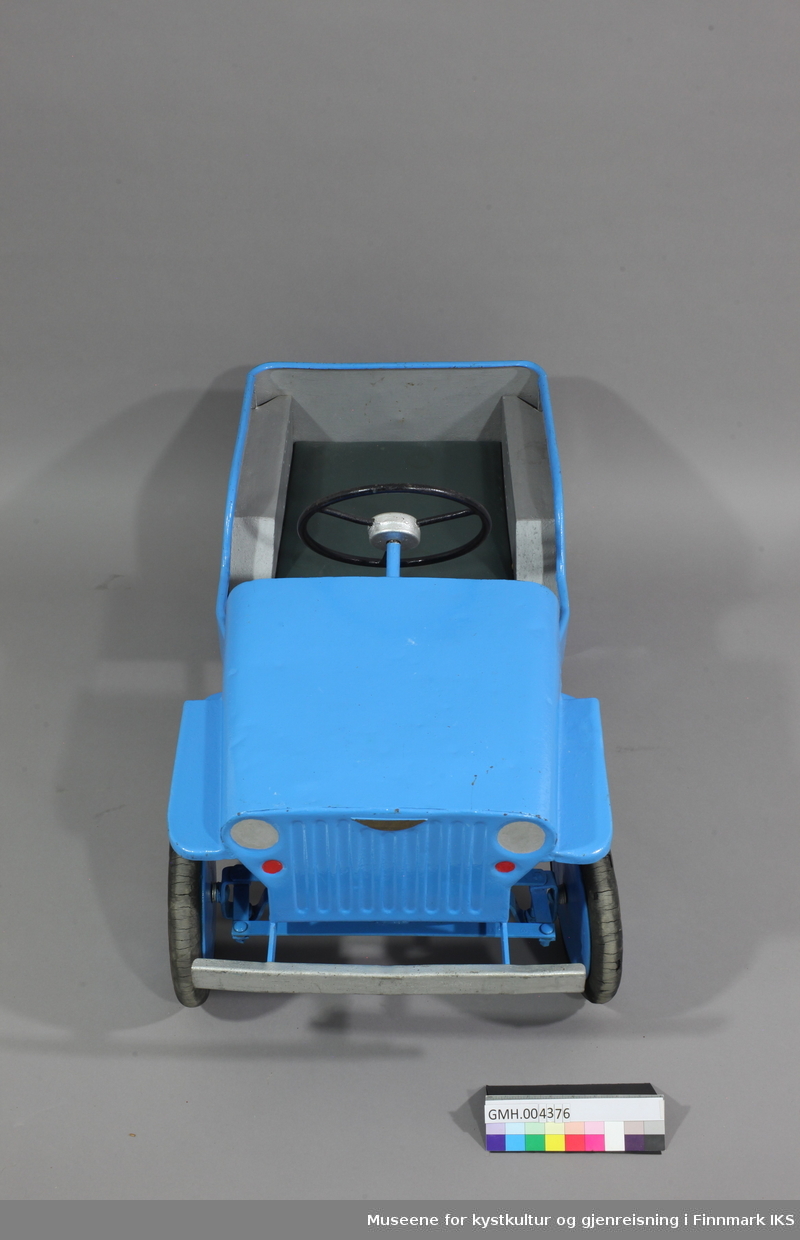 Den blåe tråbilen er laget av metall og formet som en jeep. To pedaler under driver framhjulene. Foran er det en sølvfarget støtfanger og  det er tegnet inn frontlys i samme farge.Setetrekket er av grønt kunstskinn. Innsiden av bilen er sølvfarget.