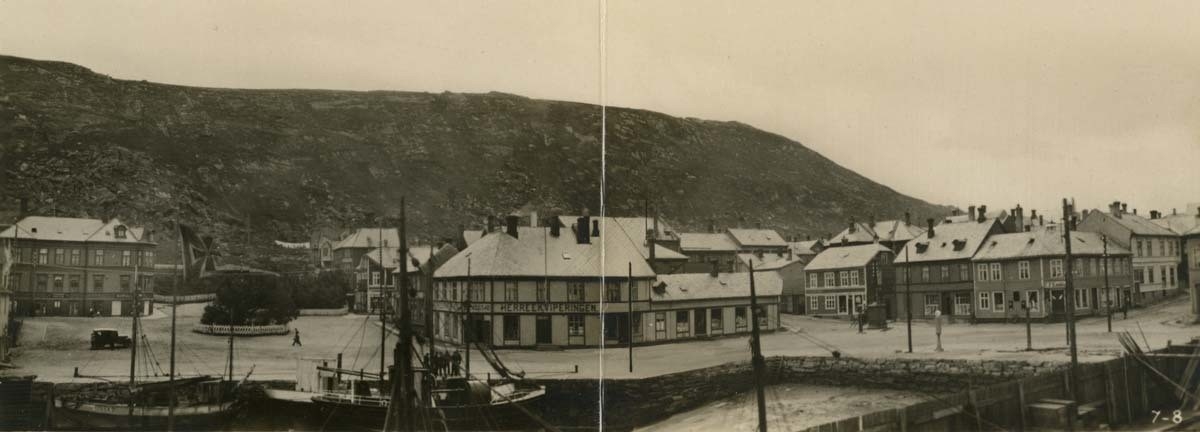 Ovsiktsbilde av Hammerfest sentrum før ødeleggelsene under andre verdenskrig. Man ser havna med båter i foprgrunn, bankbygget, andre foretninger, Oscars plass, en bil, fotgjengere og salenfjellet i bakgrunnen.