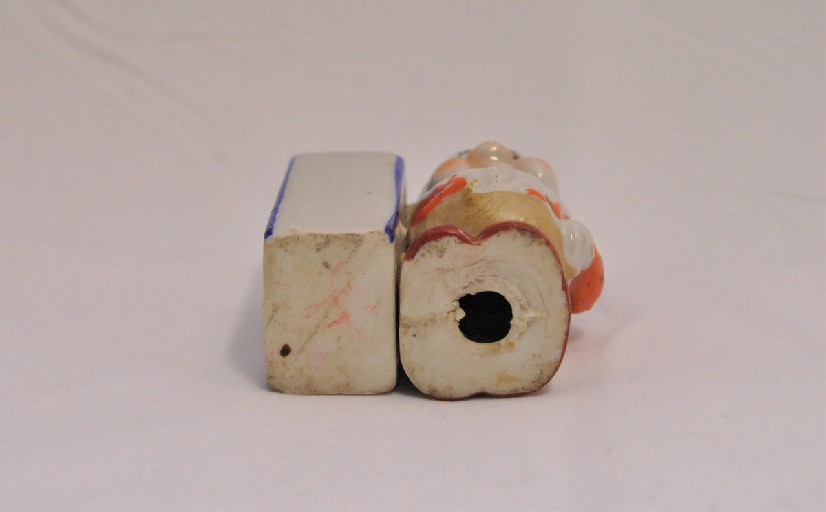 Liten figur i form av en av dvergene fra Snehvit (Blygen?) i porselen. På sin høyre side har han en firkantet beholder, mest sannsynlig til oppbevaring av tannpirkere.