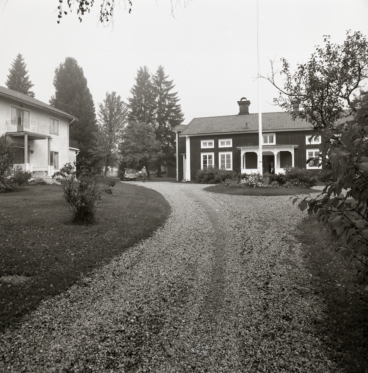 En grusväg leder fram till två bostadshus. Framför husens förstukvistar finns en gruscirkel med en vacker blomrabatt.