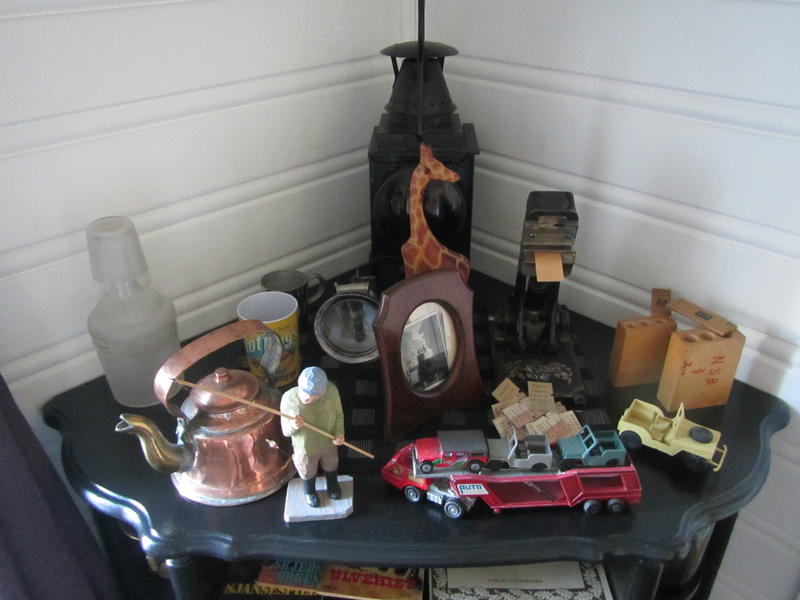 Et bord med mange gamle gjenstander - kobber kaffekjele, lekebiler, sjiraff, bilder