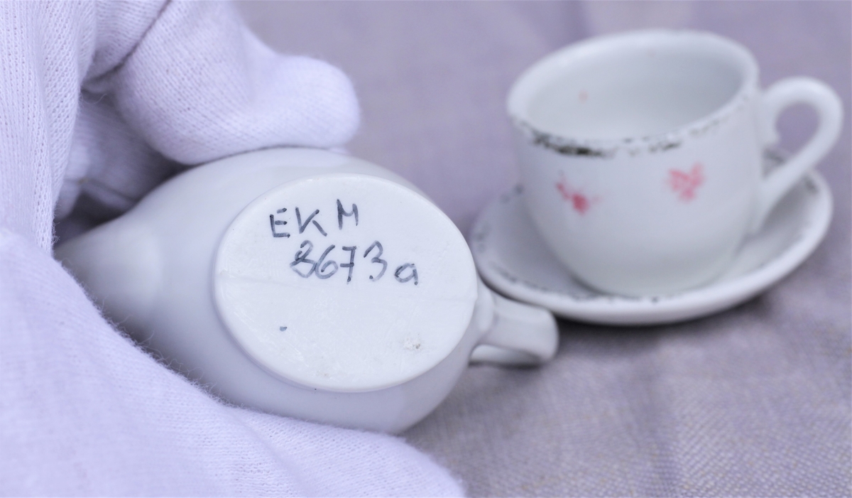 Kaffekanne (a), kopp (to) og skål i hvitt stentøy med påmalt blomst. Koppene har noen rester av rand, litt rødt.