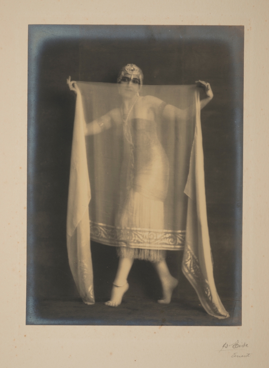 Kunstnerisk portrett av den berømte russiske ballettdanseren Vera Fokina, med et gjennomsiktig sjal foran seg.
Fra 'Salome - De syv slørs dans'.
