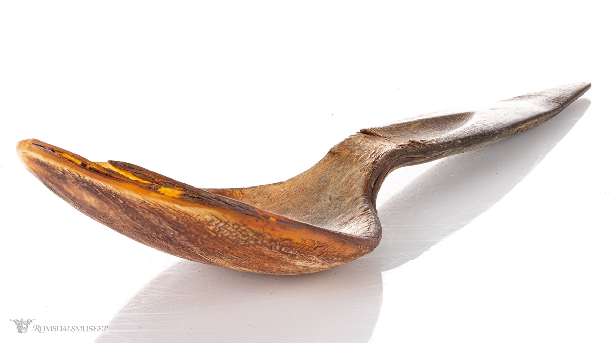 Skje av presset horn med bredt ovalt skjeblad som er spisset i endenSkaftet har et skåret spor fra bladet og midt opp på skaftet som ender i en spiss.