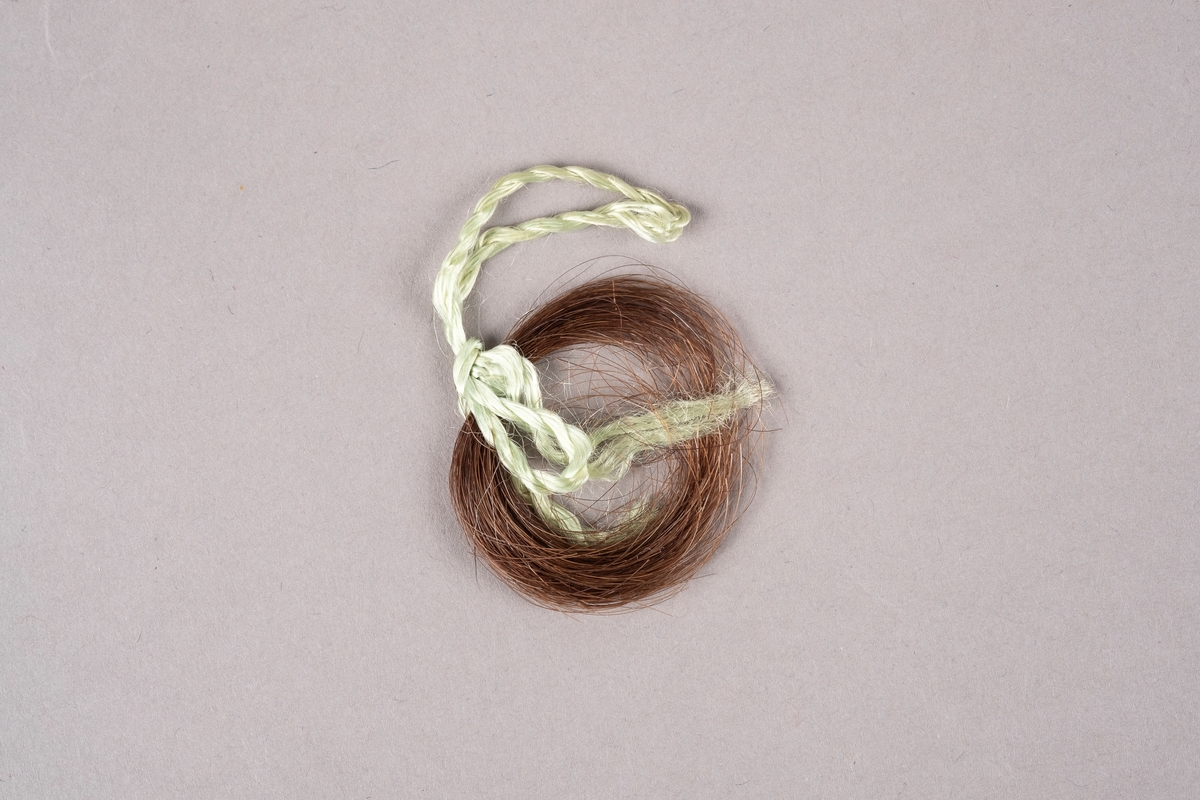 En hårlokk bundet med grønn tråd.