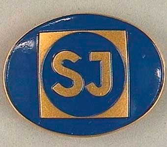 Tjänstetecken av metall i form av en liggande oval med SJ:s logotyp i guld mot blå botten.