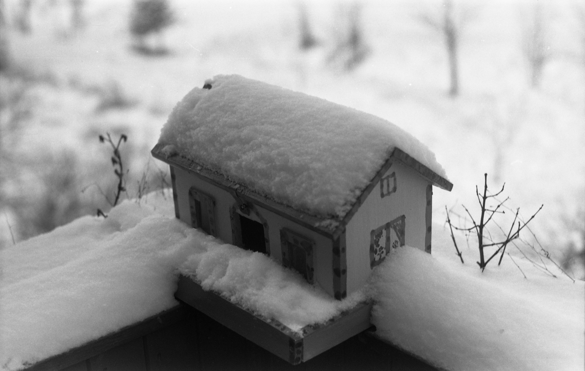 Fuglebrett utformet som miniatyrhus. Vintermotiv.