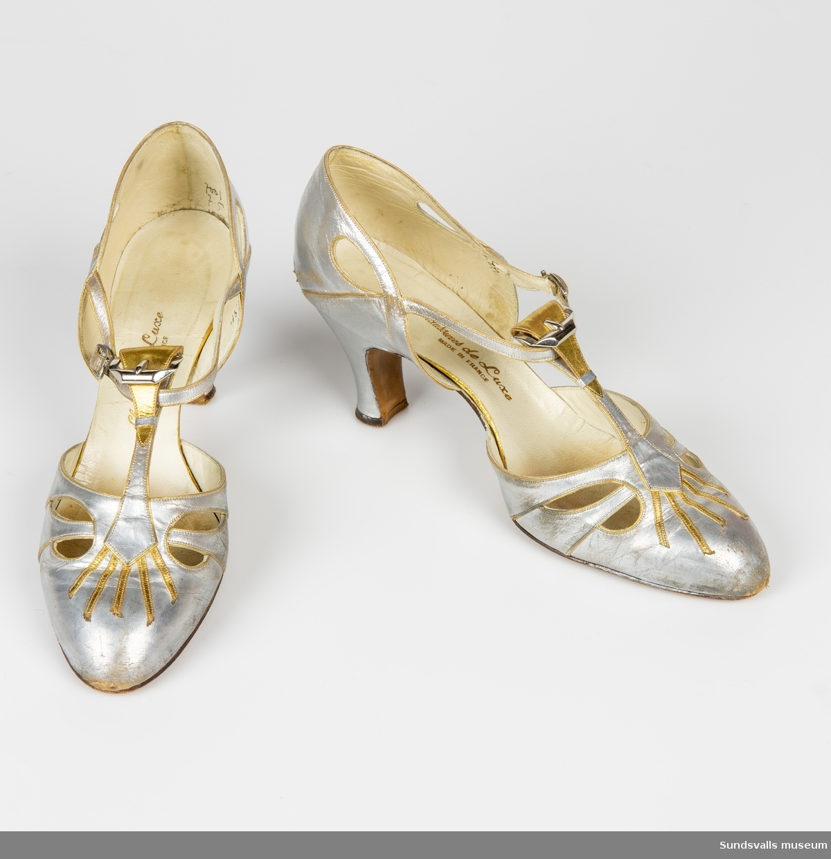 Ett par silverfärgade damskor med gulddekoration. Sleif, hög smal klack. Märkning 'Chaussures de Luxe Made in France'.