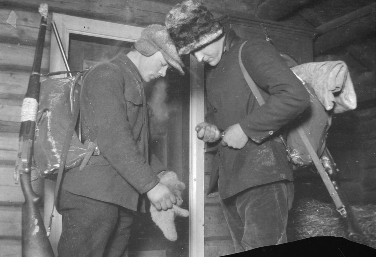Karl Sannheim og Karl Ivar Moe med geværer og ryggsekker, inne i en bu.