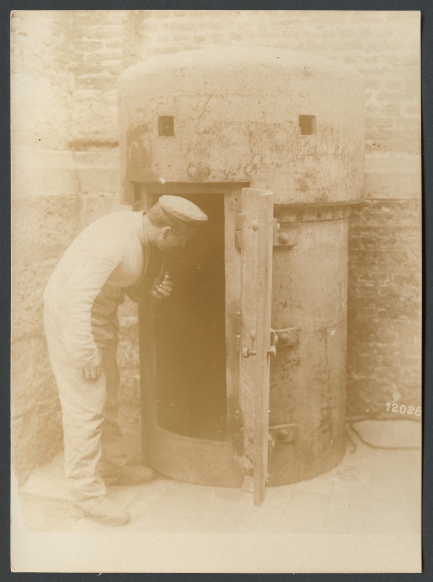 Bilden visar hur en man i arbetskläder tittar in i ett skyddsrum i stål för en person.