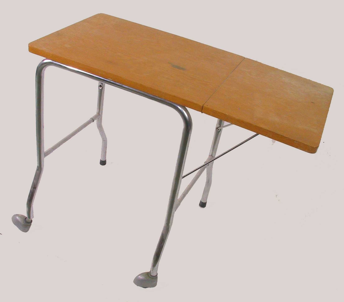 Lite bord av eikefinert plate og stålrørben. Med hengslet sideplate og hjul under to bein.