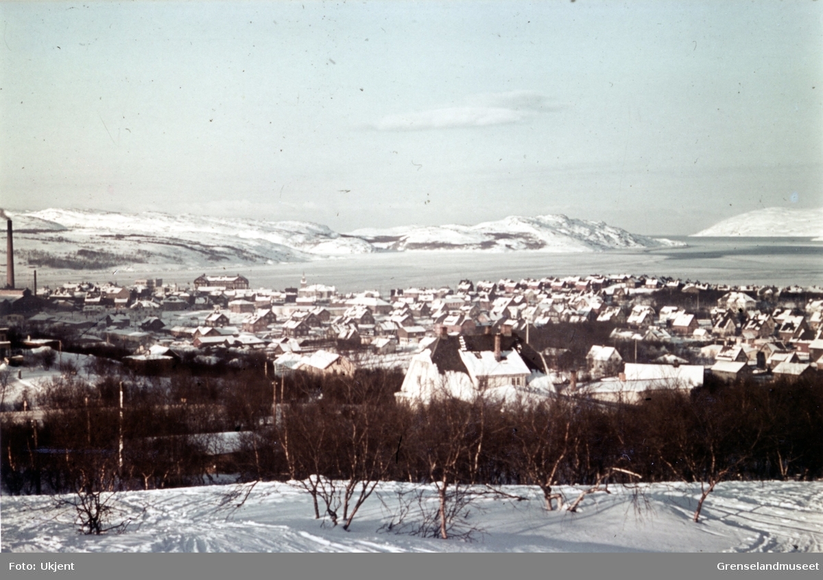 Kirkenes sett fra Prestefjellet. Fra venstre i bildet ser vi Dampsentralen, betongskolen, skolen og så kirken. Fjorden har et tynt islag.