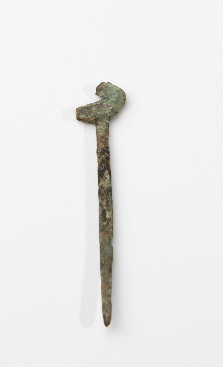 Dräktnål av brons med C-format huvud. Påträffad i grav A25. Nålen liknar vagt så kallade fågelnålar, men denna saknar i så fall huvudet.