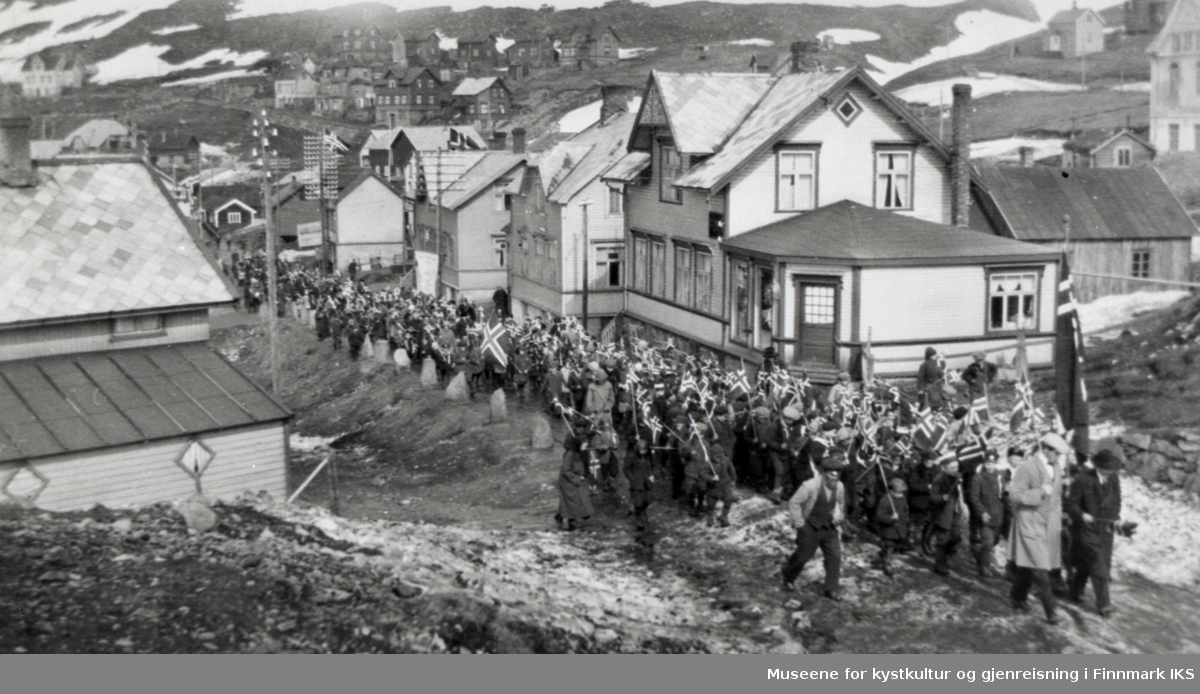 Honningsvåg. 17. mai-tog i "Skjæringa". Det nærmeste hus på høyre side tilhørte Rolf Christian Olsen. 1930-årene.