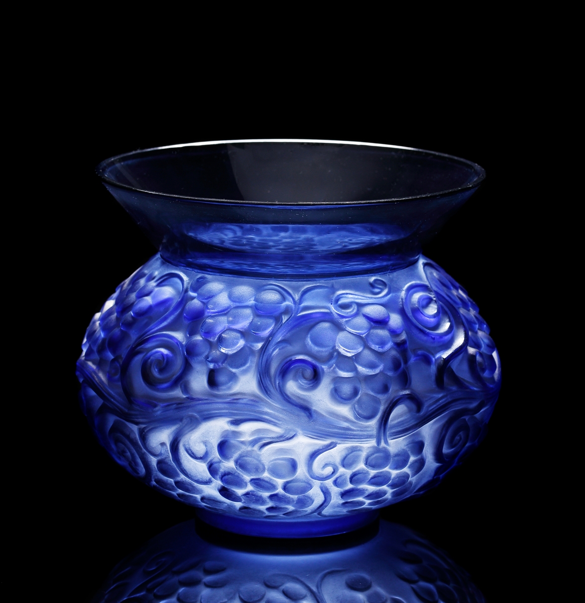 Halvopak blå vas med reliefmönster föreställande vinrankor. Utsidan till större delen matt, medan insidan är blank.