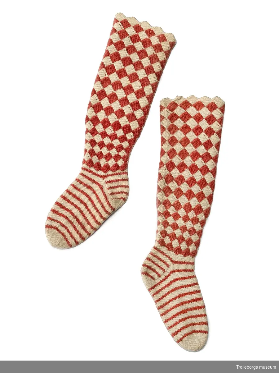 Ett par handstickade barnstrumpor, skaften konststickade i vitt och rött. Själva foten på strumporna är röd- och vitrandig.
