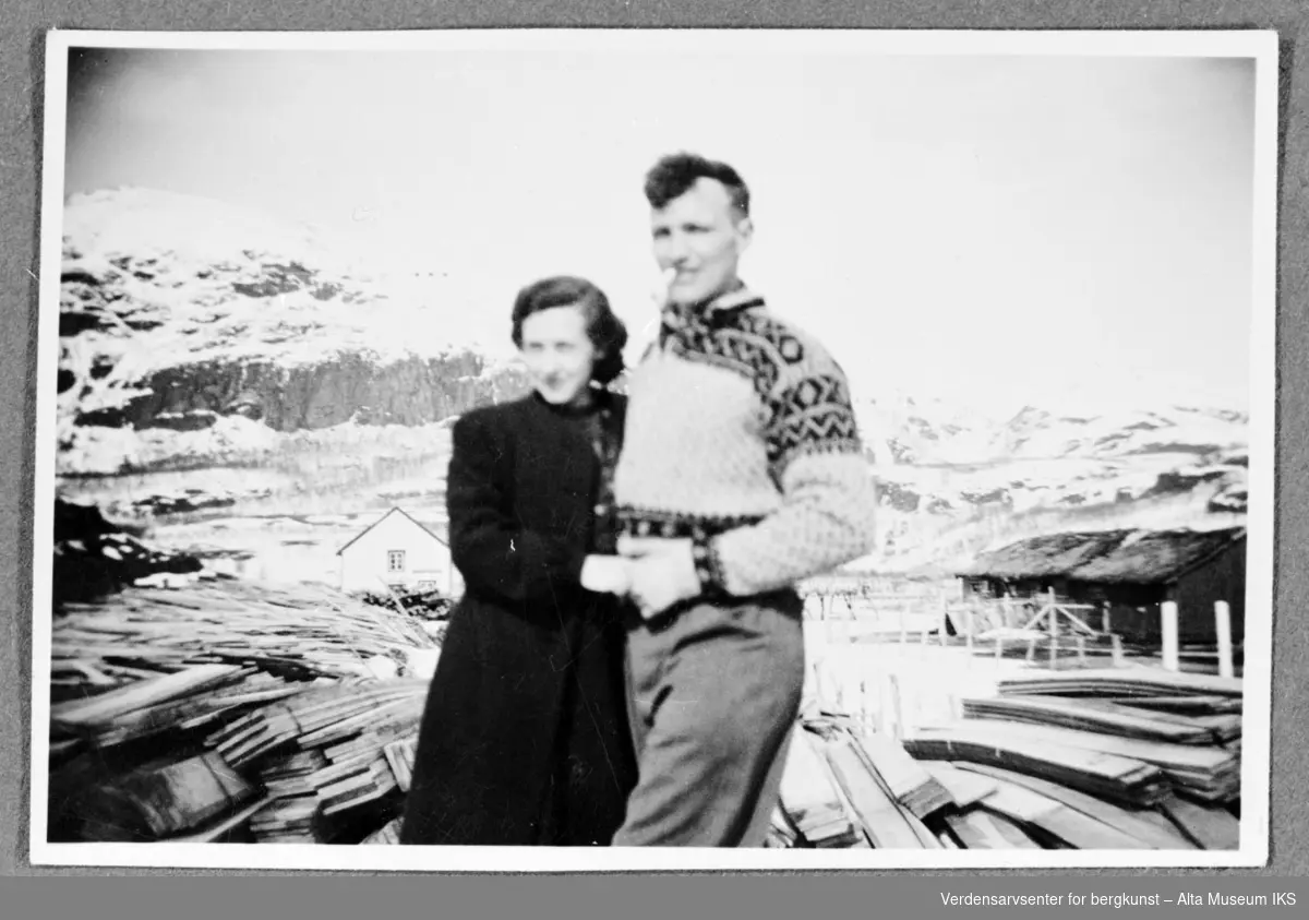 2 personer bak et tysk materiallager med planker og snødekte fjell i bagrunn.