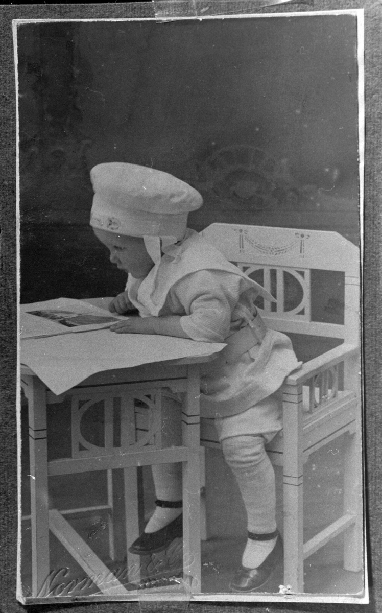 Studioportrett av barn sittende ved et bord. Barnet ser i en billedbok.