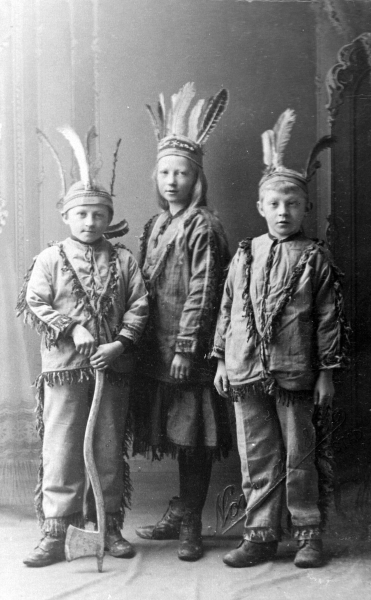 Studioportrett av tre søsken i indianerkostymer.