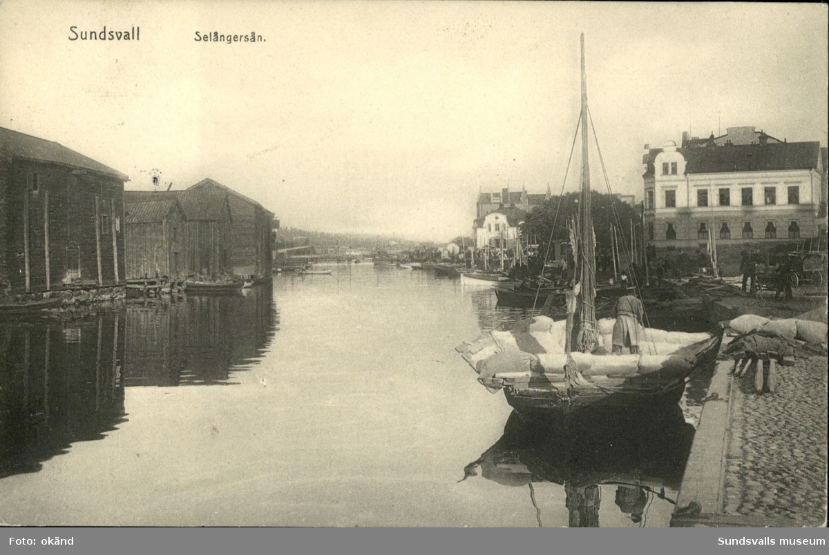 Vykort med motiv över Selångersån i Sundsvall. I förgrunden en båt lastad med säckar.