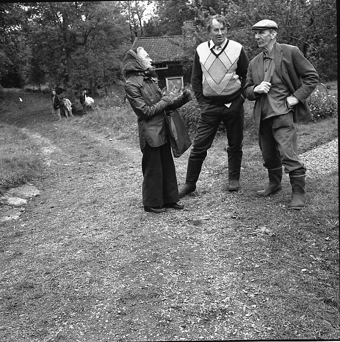 Tre okända personer, en kvinna och två män, står vid en mindre grus/gräsväg.