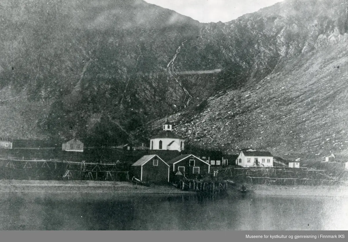 Handelstedet Kjelvik med kai, bolig, pakkhus og fiskehjeller. Kjelviks gamle åttekantete kirke (1844-1882) i bakgrunnen. Før 1882.