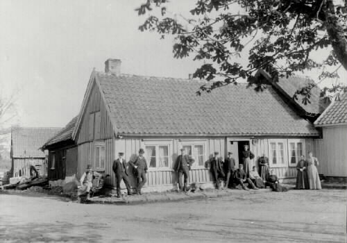 Törngrens gamla boningshus i hörnet av Krukmakaregatan och Lilla torg, rivet 1905. På trappan sitter C L Törngren och hans hustru Sofia. T v närmast trappan står sonen Hans. De tre stående männen , två av dem är guldsmeder, är söner till guldsmed C P Pettersson.
