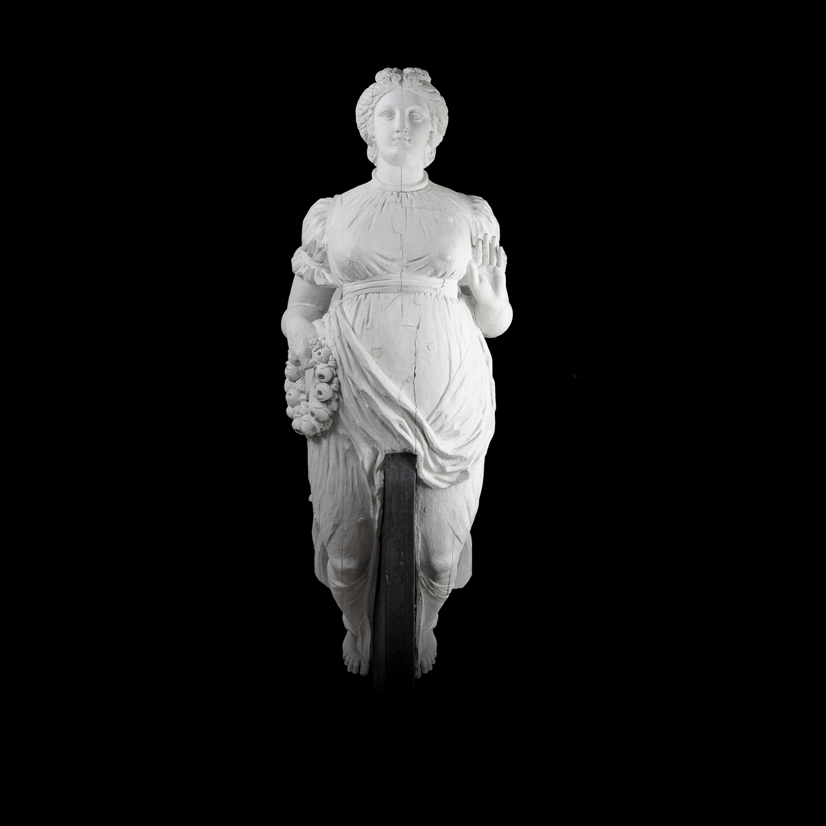 Galjonsbild tillhörande fregatten Fröja.
Kvinnofigur med blomsterkrans i högra handen. Vänstra armen hålls framåt i midjehöjd med handflatan framåt/uppåt. Figuren bär klänning med hög åtsnörd midja, åtsnörd vid överarmar och hals.