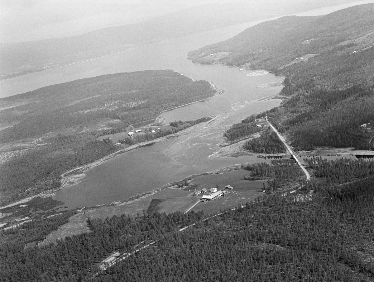 Tømmer i Valmen, ei vik i den nordvestre enden av Osensjøen i Åmot kommune i Hedmark. Hit ble tømmer fra området rundt sjøen buksert ved hjelp av slepebåten Trysilknut, for det er fra Valmen det rennende vannet i elva Søndre Osa skulle føre tømmeret videre i retning av elva Rena og Glommavassdraget. Osdammen, der tømmeret ble tappet ut fra sjøen, lå ved den høyre ytterkanten av dette bildet. I forgrunnen ser vi ned på garden Valmsneset. Vi ser også fylkesveg 2158, som går på den bortimot 24 kilometer lange strekningen mellom Valmen i Nordre Osen og Sjøenden i Søndre Osen. Osensjøen er 28 kilometer lang og har et vannspeil som er 47 kvadratkilometer stort. Tilsiget av vann kommer fra et nedslagsfelt på om lag 1 300 kvadratkilometer, hvorav om lag halvparten er dekt av produktiv skog. Flyfoto.
