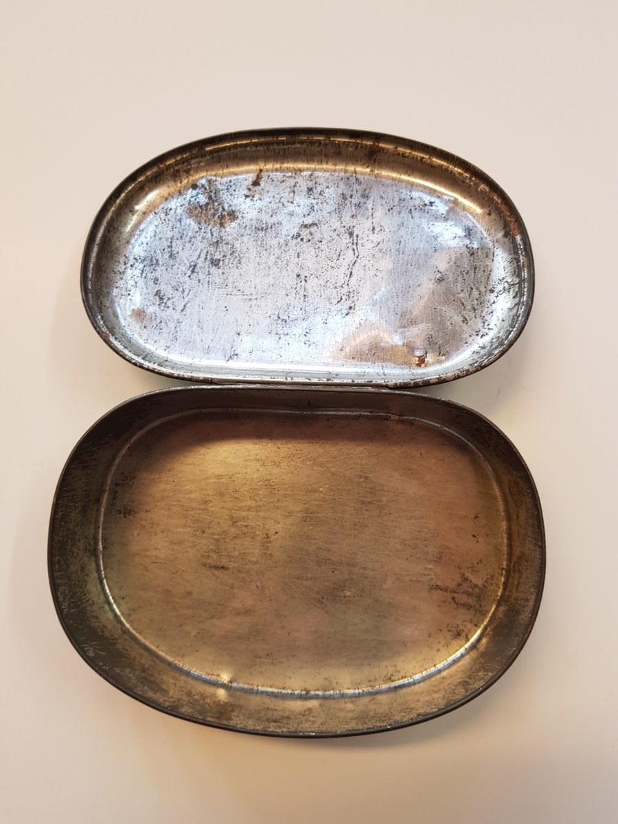 Hengslet oval boks i metall med dekor på lokk